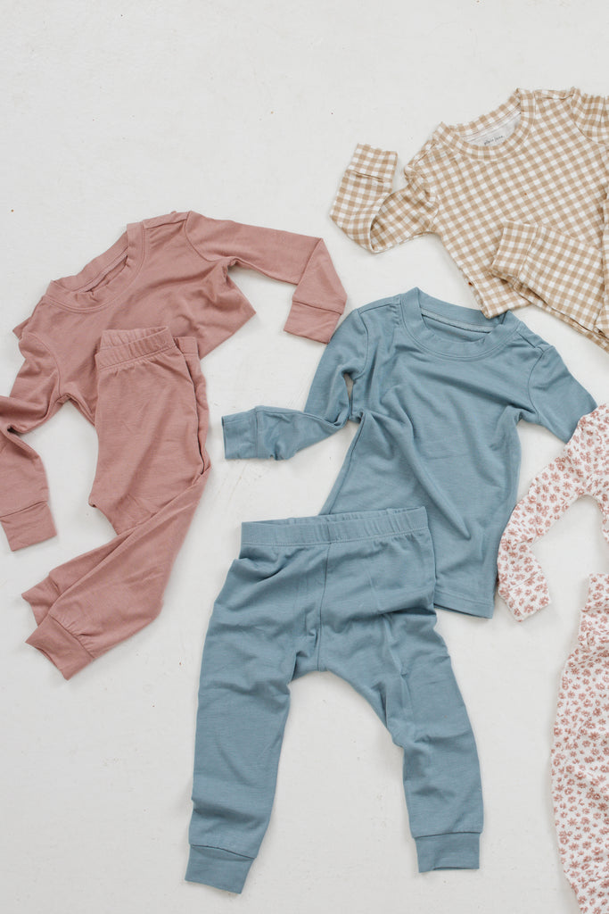 Flat lay photo of kids' PJ sets laid out on a white backdrop. Featuring dusty rose, mineral blue, birch gingham, and mauve floret.