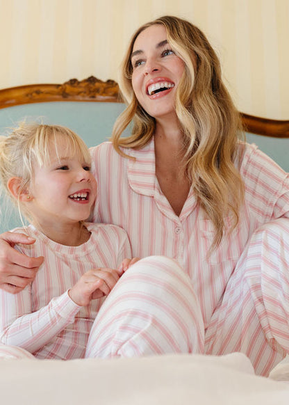 Woman and child in matching pink striped pajamas sitting on a bed.
